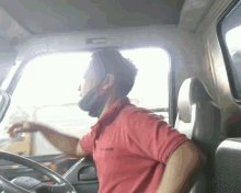a man wearing a red shirt and a black mask is driving a truck