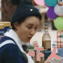 a woman is sitting at a table with balloons in the background and a bottle of alcohol .