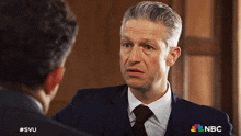 a man in a suit and tie is talking to another man with a nbc logo on his shirt