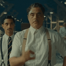a man with a bandage on his head stands next to another man with suspenders