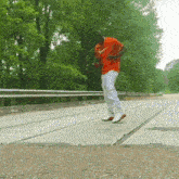 a man wearing an orange nike shirt and white pants is walking on a road