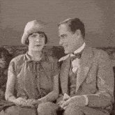 a man and a woman are sitting on a couch and the woman has a hat on