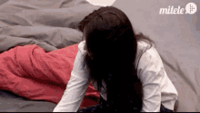 a woman is laying on a bed with a red blanket and a grey comforter .