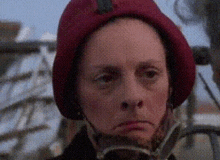 a woman wearing a red hat is looking at the camera with a serious look on her face .