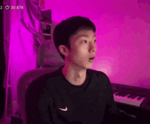 a young man is sitting in front of a keyboard in a room with purple lights behind him .