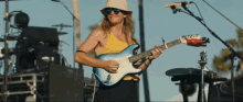 a man wearing a hat and sunglasses is playing a guitar on stage