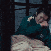 a man in a green shirt is laying in bed with a blanket on .
