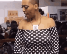 a woman wearing a black and white polka dot off the shoulder top is standing in front of a crowd of people .