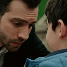 a man and a boy are looking at each other and the boy is wearing a blue jacket