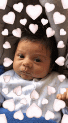 a baby is surrounded by pink hearts and looking at the camera