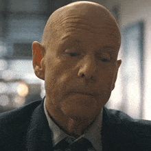 a bald man in a suit and tie looks down