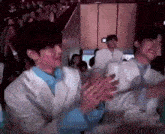 a group of young men are sitting at a table clapping their hands in a room .