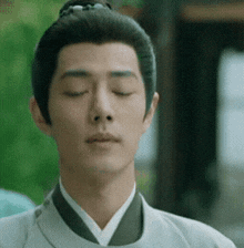 a close up of a man 's face with his eyes closed and his hair in a bun .