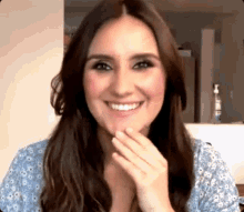 a woman with long brown hair is smiling while covering her mouth with her hand .