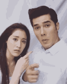 a man and a woman are standing next to each other and the woman is pointing at the man .