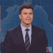 a man in a suit and tie is smiling in front of a snl sign