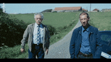 two men standing next to each other on a road with the letter g on the side of the car