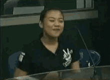 a woman in a black shirt with a peace sign on it is smiling while sitting at a desk .