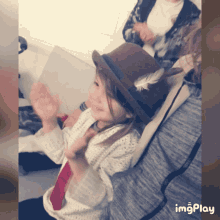 a little girl wearing a hat with a feather on it is sitting on the floor