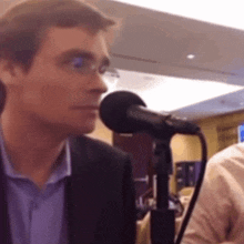 a man in a suit is speaking into a microphone while wearing glasses