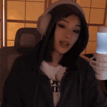 a woman wearing headphones and a hoodie is standing in front of a microphone .