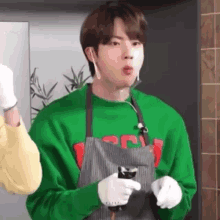 a young man wearing a green sweater and an apron is holding a bottle of water .