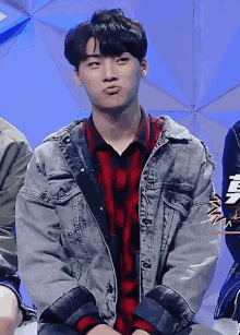 a young man wearing a denim jacket and a plaid shirt is making a funny face