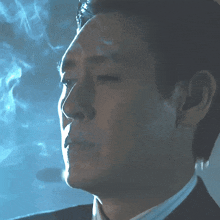 a man in a suit smoking a cigarette with smoke coming out of his mouth