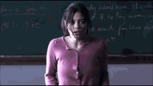 a girl in a pink sweater is crying in front of a blackboard