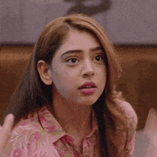 a woman wearing a pink shirt with flowers on it looks surprised