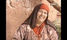 a woman wearing a head scarf is smiling in front of a wall with a sign that says vm production