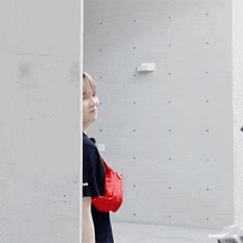 a person is peeking out from behind a wall with a red bag on their back .