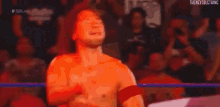 a wrestler is kneeling down in a wrestling ring with his arms outstretched in front of a crowd .