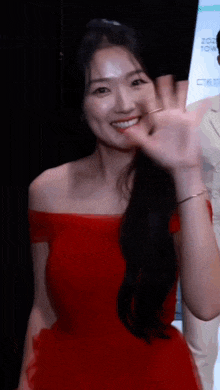 a woman in a red off the shoulder dress is waving