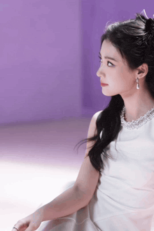 a woman wearing a white dress and earrings is sitting in front of a purple wall .