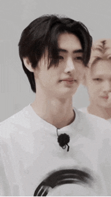 a young man wearing a white t-shirt with a microphone on his neck is looking at the camera .