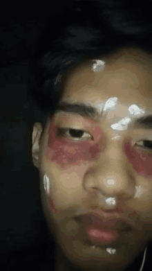 a close up of a man 's face with red eyes and white spots on his forehead .