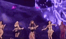 a group of women are dancing on a stage with a purple background .