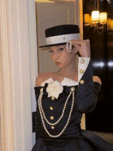 a woman wearing a hat and pearls is standing in front of a door .