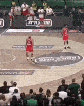 a group of people are watching a basketball game on a court with a sponsor 's logo on it