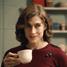 a woman with a brooch on her shoulder is drinking from a white cup