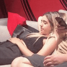 a woman is laying on a man 's lap on a couch and looking at her phone .