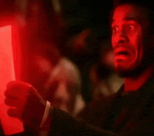 a man is holding a piece of paper in front of a red light and making a surprised face .