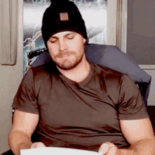 a man wearing a black beanie is reading a piece of paper