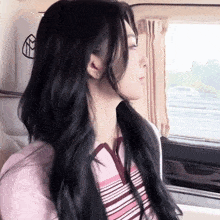 a woman with long black hair is looking out a car window