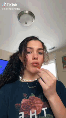 a girl with curly hair is wearing a floral shirt and a pearl necklace while eating a strawberry .
