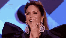 a woman wearing a black dress and earrings is smiling and clapping