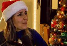 a woman wearing a santa hat is sitting in front of a christmas tree and talking into a microphone .