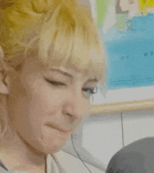 a woman with blonde hair is smiling and looking at the camera in front of a painting .