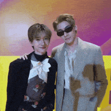 a man in a suit stands next to another man wearing sunglasses